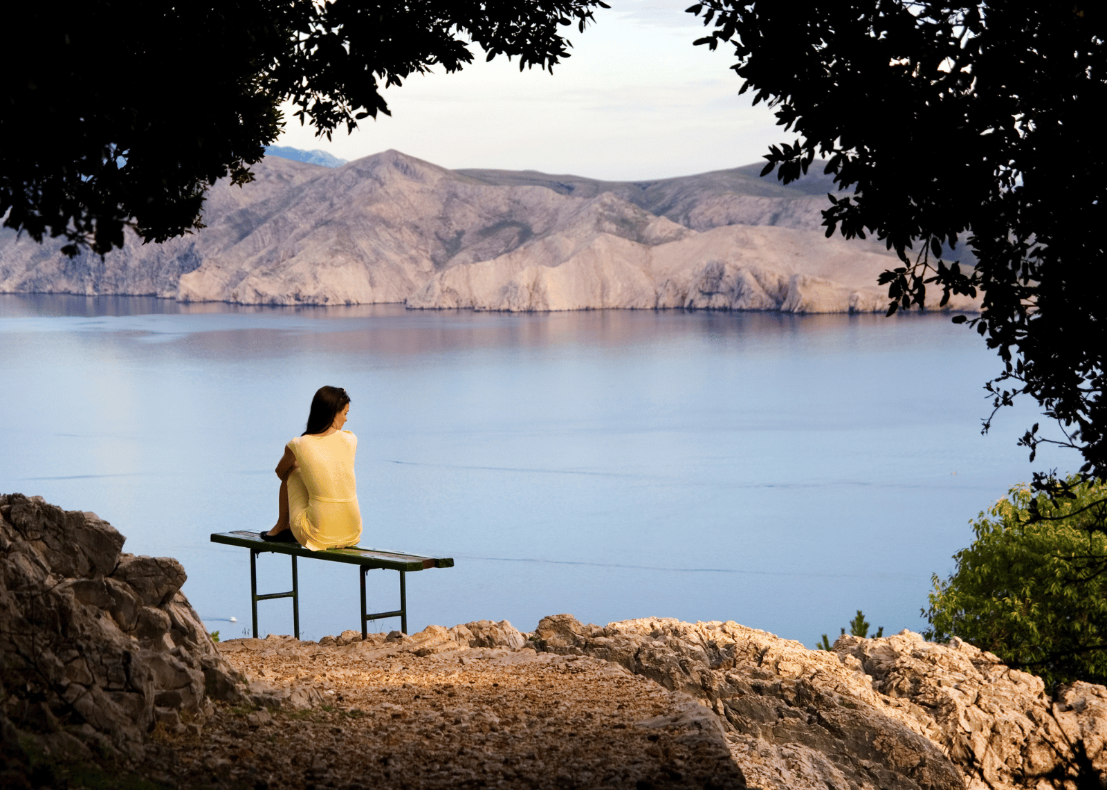 A lonely girl sitting near a mountain seaside, deep in thought.